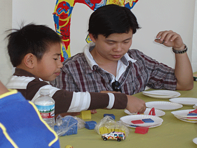 De Anza College student intern Minh Nguyen teaches 2nd grader Duc Vo how to make dancing figures out of modeling clay at Euphrat Museum's Lunar New Year Unity Parade and International Fair booth.